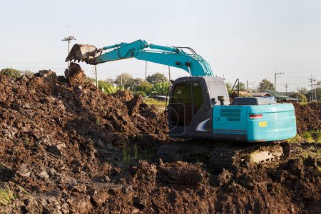 Foto de Excavadora retroexcavadora que trabaja en la excavación de un suelo para ajustar las áreas poscosecha en los campos de arroz. maquinaria agrícola para la industria agrícola moderna. - Imagen libre de derechos