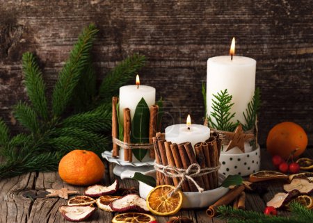 Burning Christmas or advent candles decorated with natural material. Slices of fresh dried apple, orange and spices for cooking or baking. Rustic style.