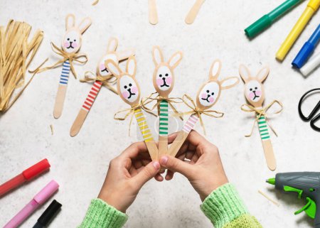 Draufsicht auf drei handgefertigte bunte lustige Hasen aus Holzlöffeln in Kinderhänden. Kleines Geschenk oder Dekor zu Ostern. Einfaches Kinderbastelkonzept.