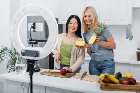 Photo for Cheerful interracial friends cutting fruits near blender and smartphone in kitchen - Royalty Free Image