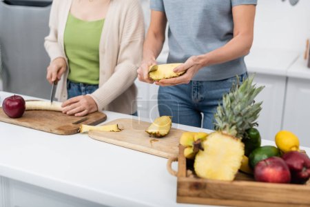 Foto de Vista recortada de amigos cortando frutas frescas en la cocina - Imagen libre de derechos