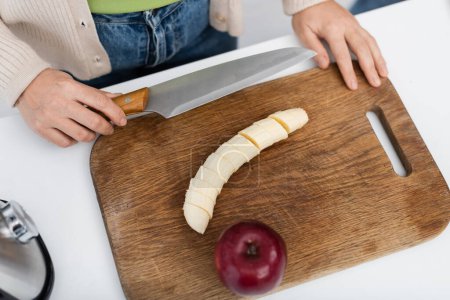 Vista superior de la mujer sosteniendo cuchillo cerca de plátano y manzana en la tabla de cortar 