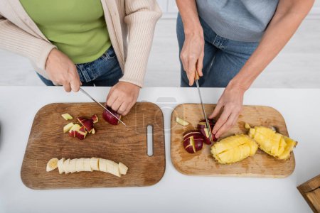 Foto de Vista superior de amigos cortando frutas frescas en tablas de cortar en la cocina - Imagen libre de derechos