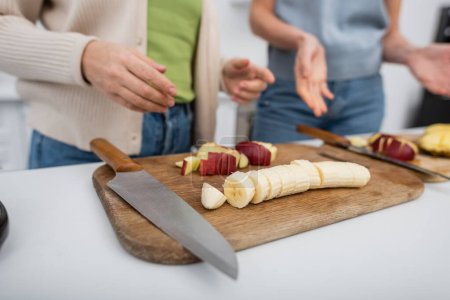 Foto de Vista recortada de frutas maduras en tablas de cortar cerca de mujeres borrosas en la cocina - Imagen libre de derechos