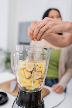 Mujer madura exprimiendo limón mientras prepara batido de frutas con un amigo en la cocina 