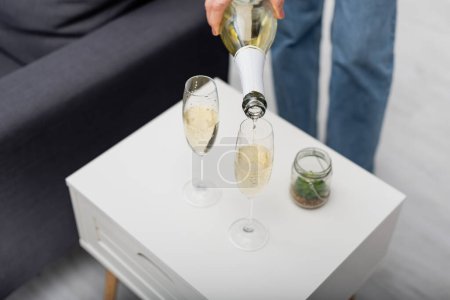 Cropped view of woman pouring champagne in glasses at home 