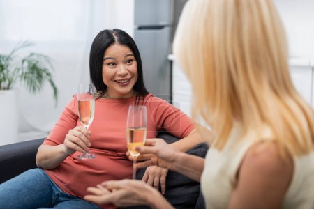 Asiatique femme parler à flou ami avec verre de champagne à la maison 