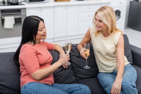 Femme d'âge moyen tenant du champagne et parlant à un ami asiatique à la maison 