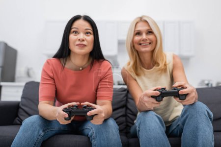 Photo for KYIV, UKRAINE - DECEMBER 2, 2021: Blurred interracial friends playing video game at home - Royalty Free Image