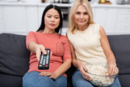 Blurred interracial amigos viendo película y la celebración de palomitas de maíz en casa 