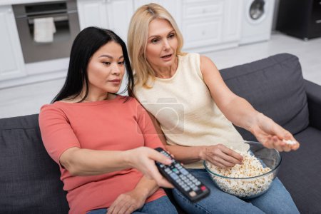 Multiethnic friends with popcorn watching movie on couch at home 