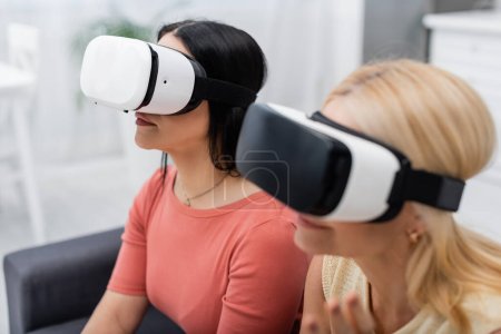Téléchargez les photos : Brunette femme en réalité virtuelle casque de jeu près de flou ami à la maison - en image libre de droit