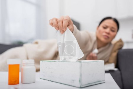 Foto de Mujer enferma borrosa tomando servilleta cerca de pastillas en casa - Imagen libre de derechos
