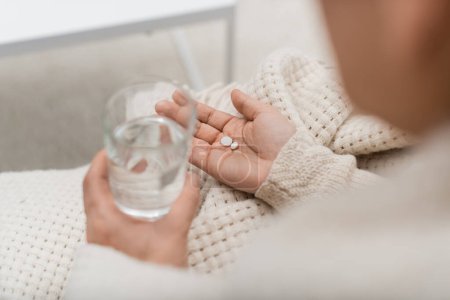 Téléchargez les photos : Vue recadrée de la femme tenant un verre d'eau et des pilules à la maison - en image libre de droit