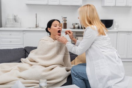 Médico con lengua depresor comprobar garganta de enfermo asiático mujer en casa 