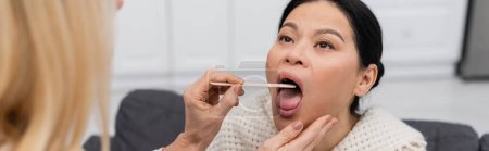Blurred doctor holding tongue depressor near asian patient with open mouth at home, banner 
