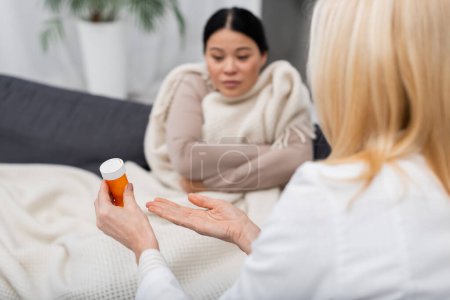 Blurred doctor pointing at pills near ill asian patient at home 