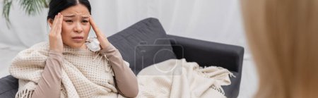 Sick asian woman holding napkin and suffering from headache near doctor at home, banner 