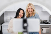 Cheerful interracial bloggers looking at blurred smartphone in ring lamp at home  t-shirt #626932300