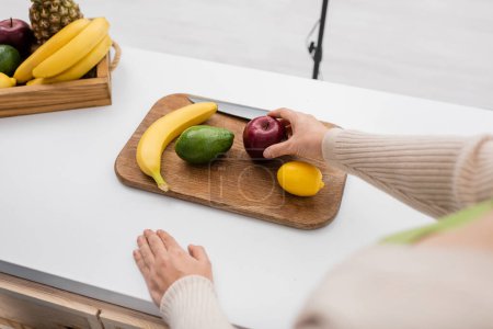 Cropped view of woman holding apple near chopping board on table 
