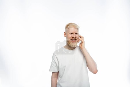 bearded albino man in t-shirt talking on smartphone and smiling on white background 