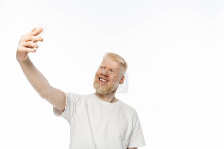 cheerful albino man in t-shirt taking selfie on smartphone on white background