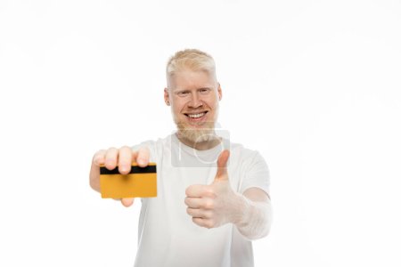 Téléchargez les photos : Heureux albinos homme tenant carte de crédit et montrant pouce isolé sur blanc - en image libre de droit