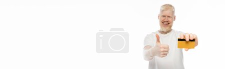 Téléchargez les photos : Heureux albinos homme tenant carte de crédit et montrant pouce vers le haut isolé sur blanc, bannière - en image libre de droit