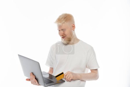 Foto de Hombre albino barbudo en camiseta con tarjeta de crédito y el uso de la computadora portátil, mientras que hacer compras en línea sobre fondo blanco - Imagen libre de derechos