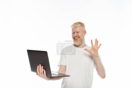happy albino man in t-shirt waving hand during video call on laptop on white background
