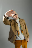 stylish albino man in sunglasses and shirt jacket posing with outstretched hand isolated on grey Stickers #627940152