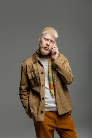 bearded albino man in stylish shirt jacket talking on smartphone isolated on grey 