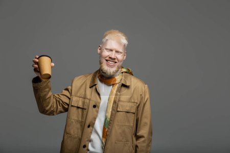 bearded and happy albino man in shirt jacket holding paper cup isolated on grey