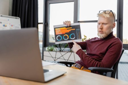 bärtiger Albino-Geschäftsmann mit Brille zeigt bei Videotelefonie auf Laptop auf Infografiken 