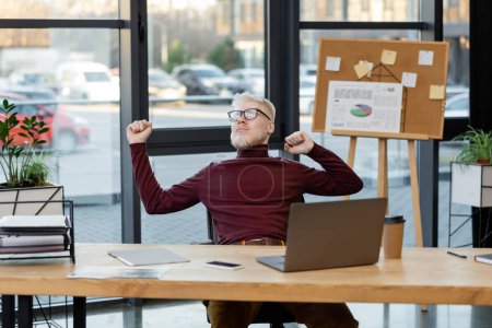 bearded albino businessman in glasses stretching near gadgets in office