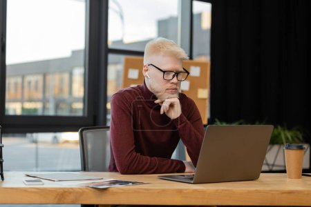 bearded albino businessman in earphones looking at laptop while working in office 
