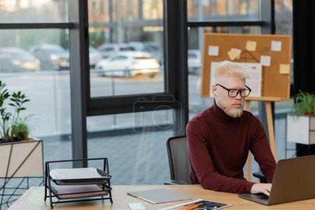 bärtiger Albino-Geschäftsmann im drahtlosen Kopfhörer mit Laptop bei der Arbeit im Büro 