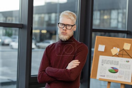Téléchargez les photos : Homme d'affaires barbu albinos dans des lunettes debout avec les bras croisés dans le bureau - en image libre de droit