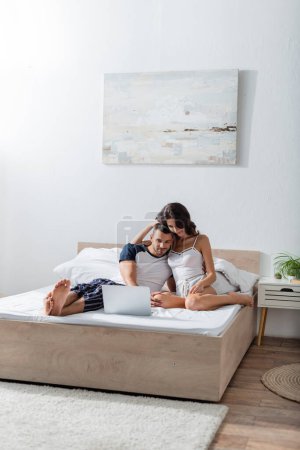 Téléchargez les photos : Brunette woman hugging brunette boyfriend in pajama on bed - en image libre de droit