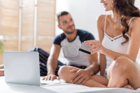 Téléchargez les photos : Blurred woman holding credit card near boyfriend on bed - en image libre de droit