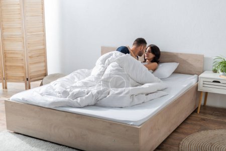 Téléchargez les photos : Bearded man kissing girlfriend on bed in morning - en image libre de droit