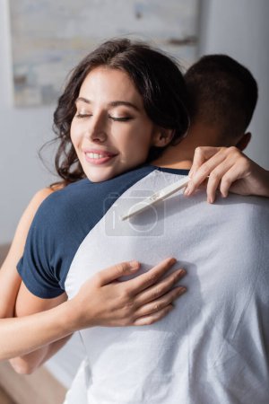 Téléchargez les photos : Positive woman holding pregnancy test and hugging boyfriend at home - en image libre de droit