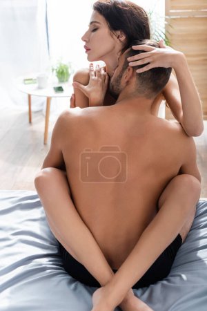 Téléchargez les photos : Muscular man kissing neck of sexy brunette girlfriend on bed in morning - en image libre de droit