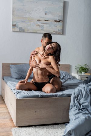 Téléchargez les photos : Bearded man touching breast of sexy girlfriend in panties on bed - en image libre de droit