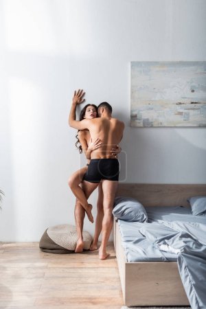 Téléchargez les photos : Muscular man in underpants kissing sexy girlfriend near bed at home - en image libre de droit