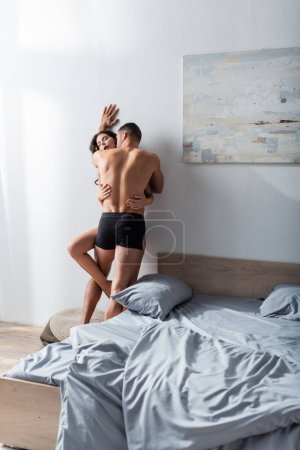 Téléchargez les photos : Muscular man kissing passionate girlfriend near bed at home - en image libre de droit
