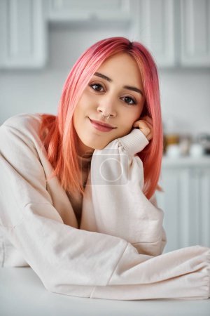 Foto de Hermosa joven con el pelo rosa en traje casual posando en la cocina y sonriendo a la cámara - Imagen libre de derechos