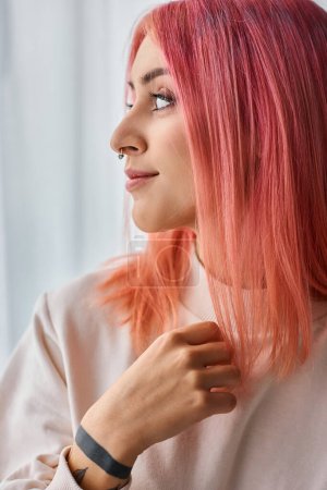Foto de Hermosa mujer joven alegre en jersey blanco con el pelo vivo rosa posando en la cocina y mirando hacia otro lado - Imagen libre de derechos