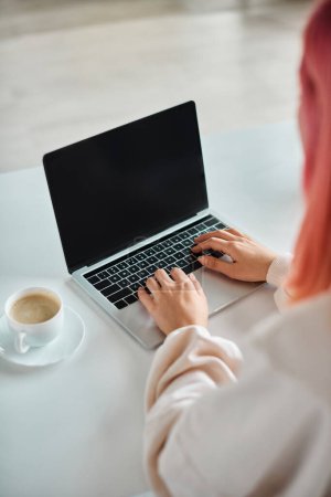 Téléchargez les photos : Vue recadrée de la femme qui travaille dur avec les cheveux roses en utilisant son ordinateur portable pour le travail dans la cuisine à la maison - en image libre de droit