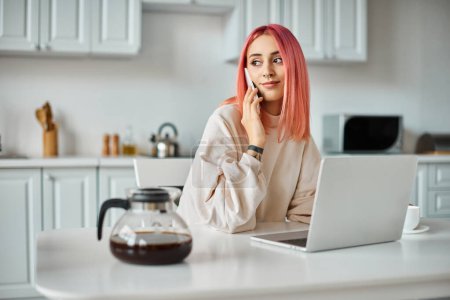 Photo for Attractive jolly woman in comfortable homewear talking by phone and looking away while in kitchen - Royalty Free Image